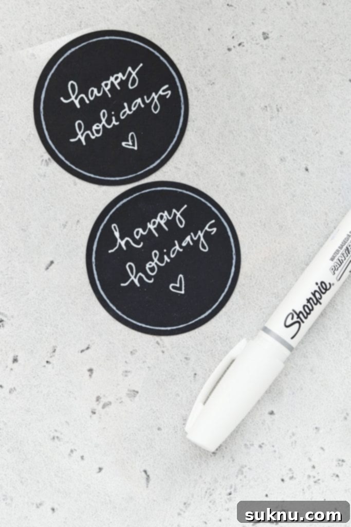 Handwritten 'Happy Holidays!' on a round chalkboard tag, often used as an optional decorative accent for gluten-free cookie gift jars.