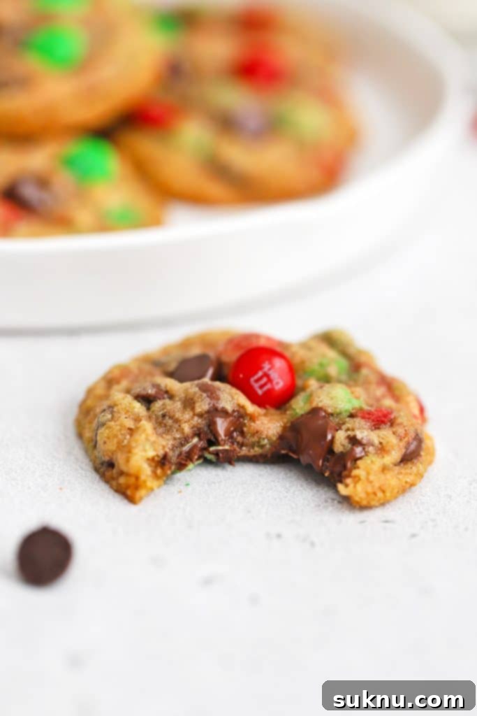 Close-up front view of a perfectly baked gluten-free M&M cookie with a bite taken out, revealing its soft, chewy interior.
