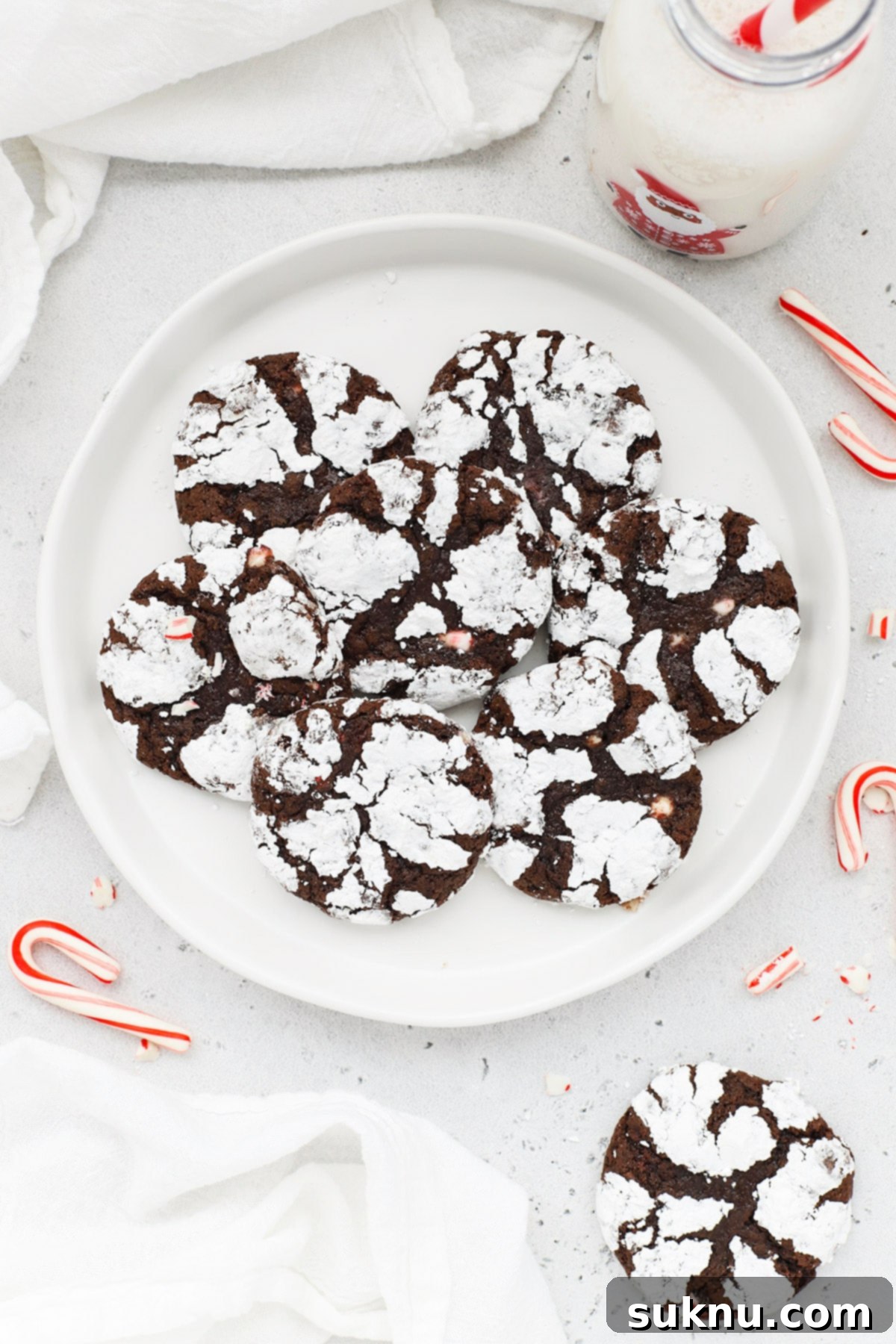 Overhead view of a plate of gluten-free peppermint chocolate crinkle cookies, dusted with powdered sugar and adorned with candy cane bits, perfect for holiday gatherings.