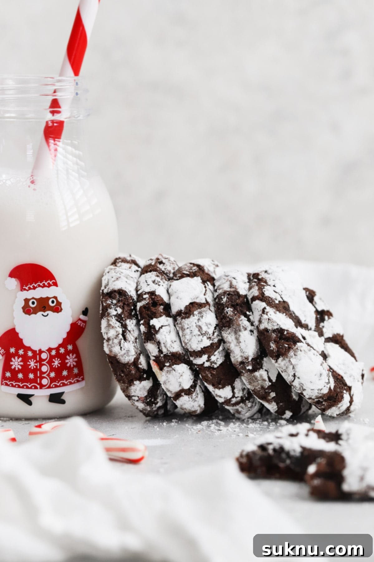 Front view of a stack of gluten-free peppermint chocolate crinkle cookies leaning on a bottle of milk, showcasing their rich color and snowy coating.
