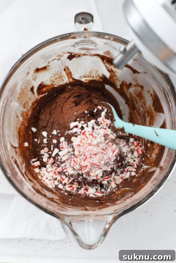 Overhead view of adding crushed candy cane into the dark, rich peppermint chocolate crinkle cookie batter.