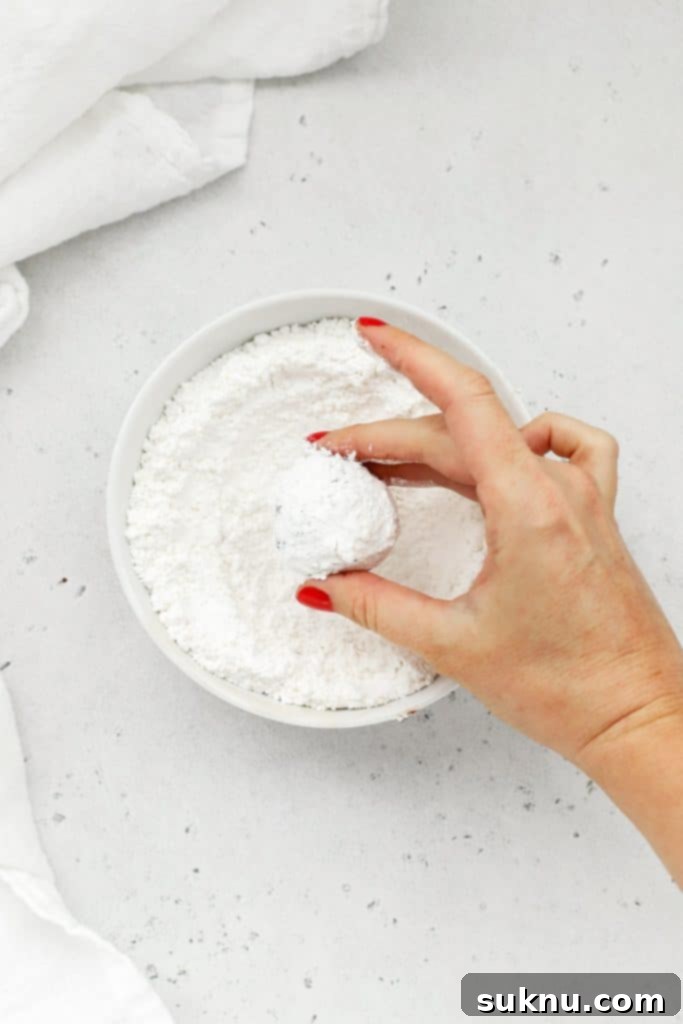 Rolling balls of peppermint chocolate crinkle cookie dough in powdered sugar, ensuring a thick, even coating.