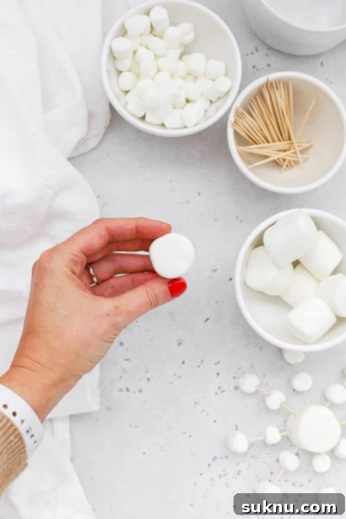 Marshmallow Snowflake Magic 5 Step-by-step image showing the first toothpick inserted into a large marshmallow.