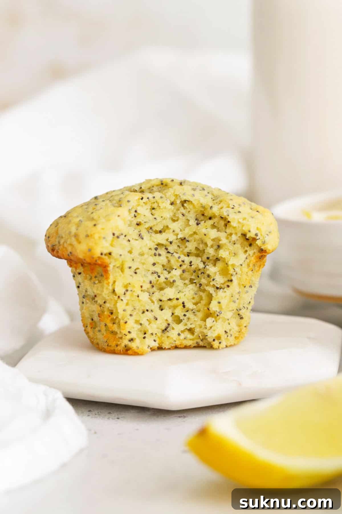 A gluten-free lemon poppy seed muffin with a bite taken out of it, revealing its fluffy interior and poppy seeds.