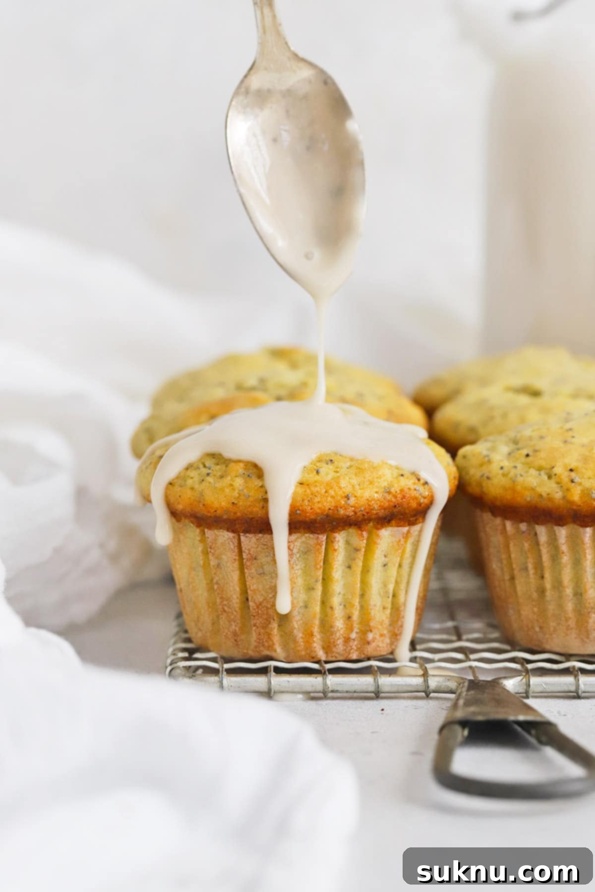 Pouring lemon glaze on gluten-free lemon poppyseed muffins, showing a luscious, sweet topping.