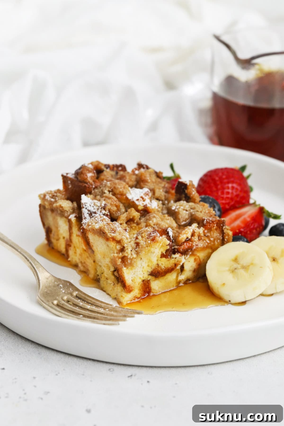 Holiday Gluten Free Eggnog French Toast Bake 2 Front view of gluten-free eggnog french toast casserole topped with powdered sugar and maple syrup, ready to be served for a delightful holiday breakfast