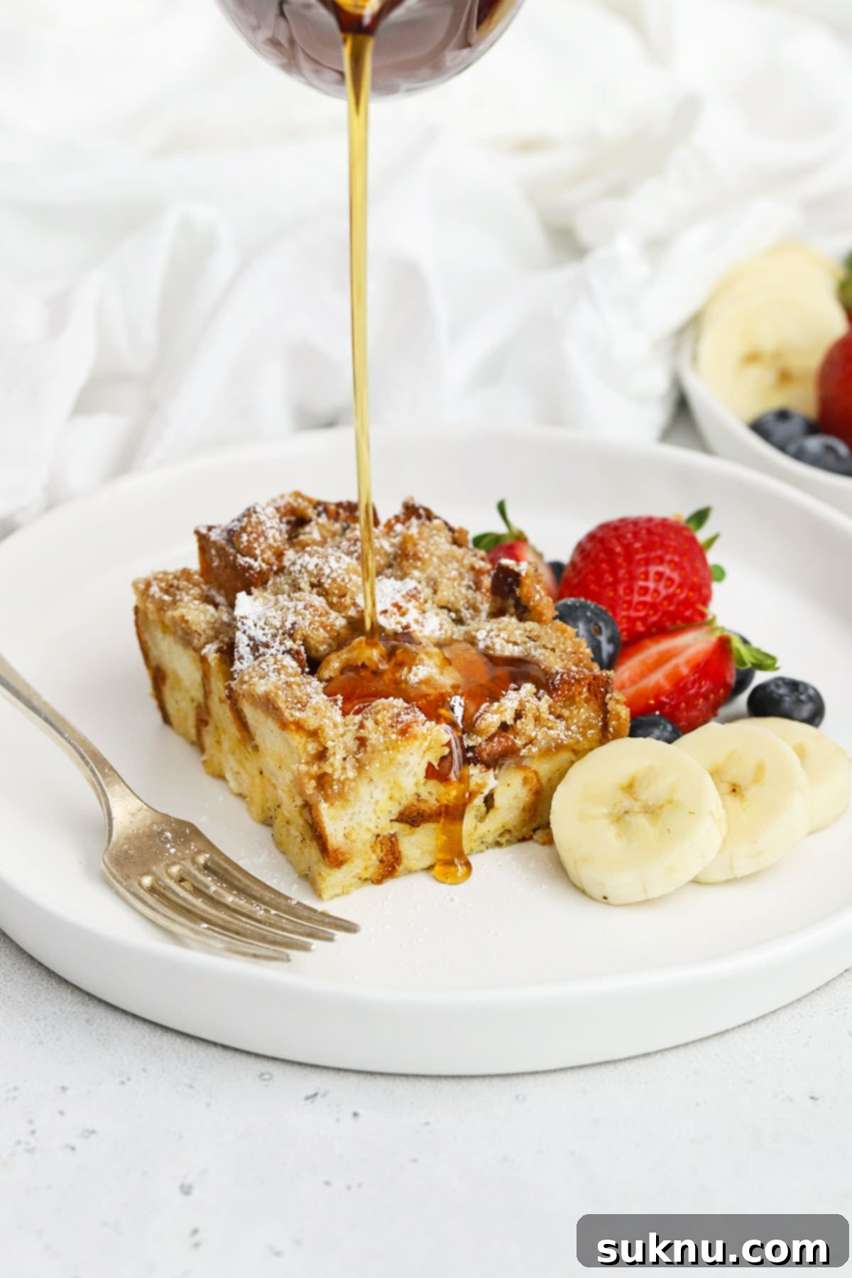 Holiday Gluten Free Eggnog French Toast Bake 14 Maple syrup being poured generously over a slice of gluten-free eggnog french toast casserole, highlighting its golden brown streusel topping