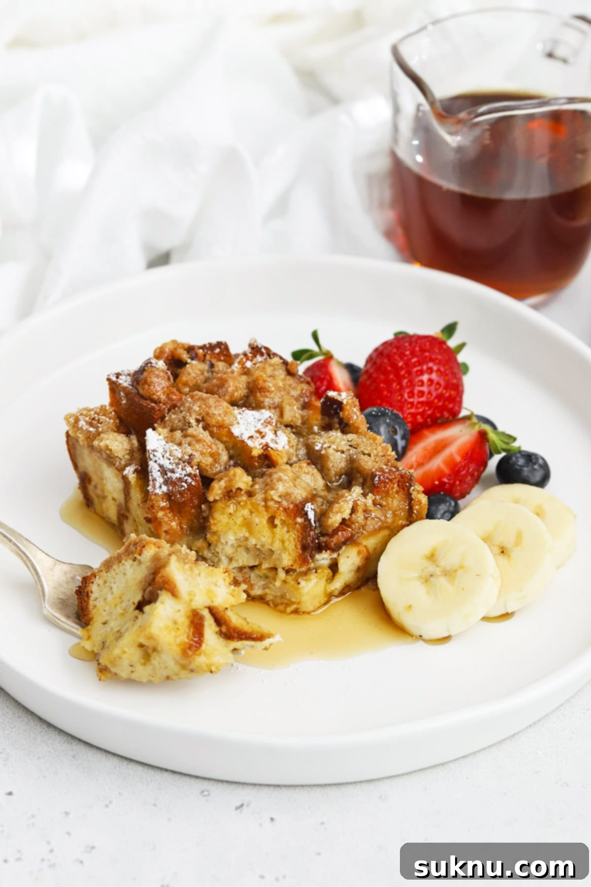 Holiday Gluten Free Eggnog French Toast Bake 15 A generous serving of gluten-free eggnog french toast casserole, topped with powdered sugar and a drizzle of maple syrup, on a white plate