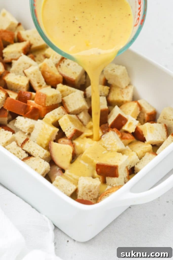 Holiday Gluten Free Eggnog French Toast Bake 6 Eggnog custard being poured over bread cubes in a baking dish, ensuring even coating for the gluten-free eggnog french toast casserole