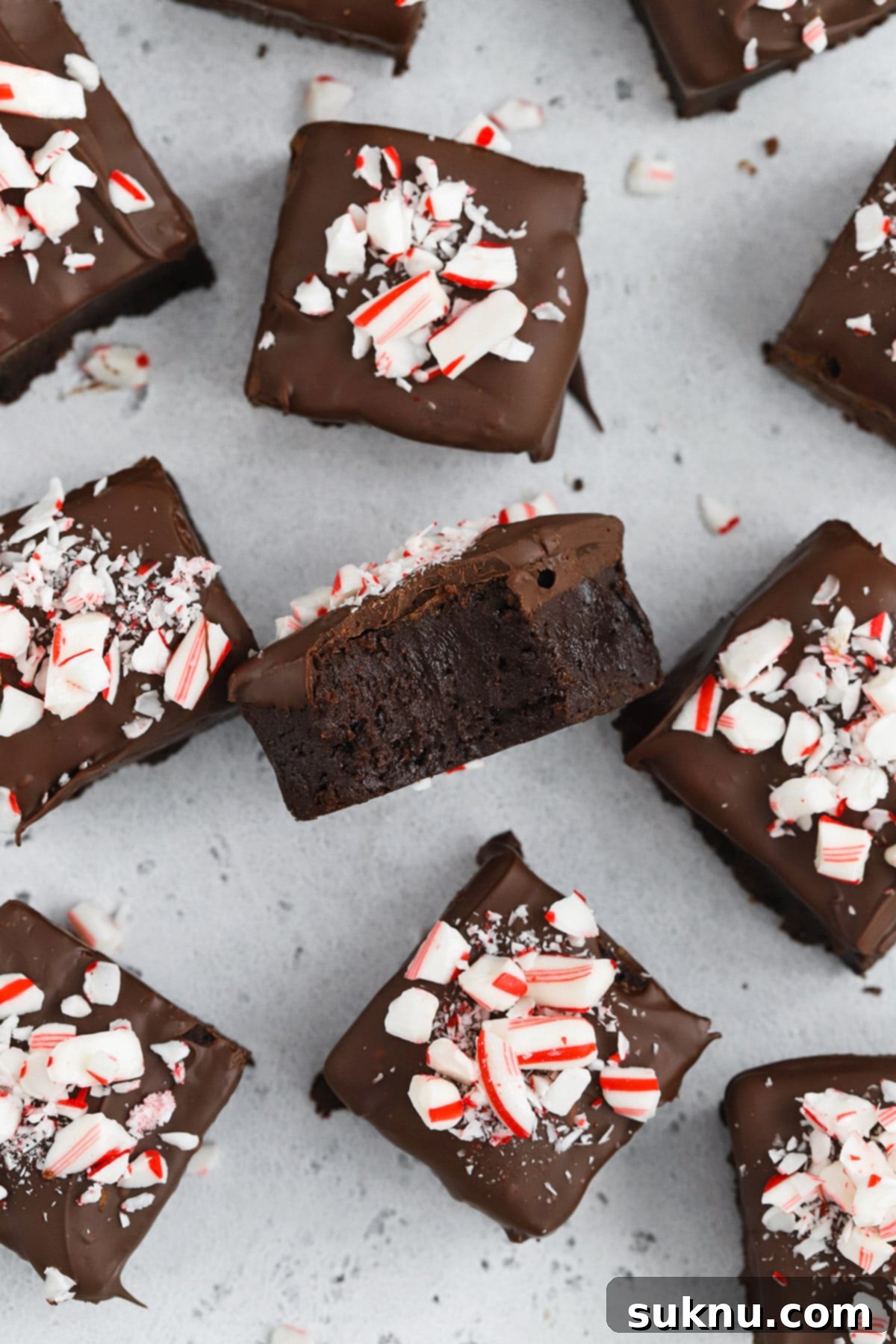 Overhead view of gluten-free peppermint brownie bites, with one piece turned to show its fudgy interior against the rich chocolate coating and candy cane sprinkles, highlighting its perfect texture.
