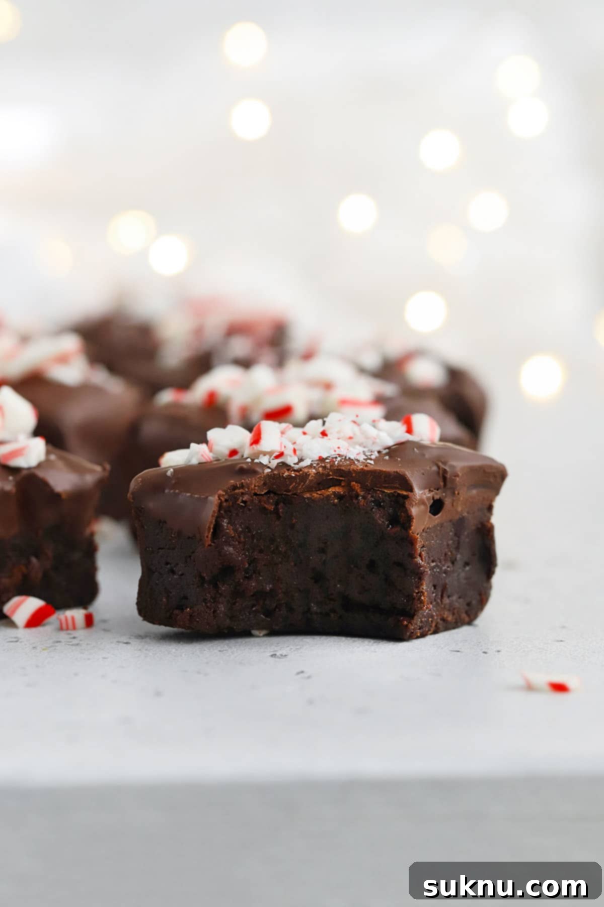 Front view of several gluten-free peppermint brownie bites. One brownie bite has a perfect bite taken out of it, revealing the soft, fudgy center contrasting with the crisp chocolate-peppermint shell.