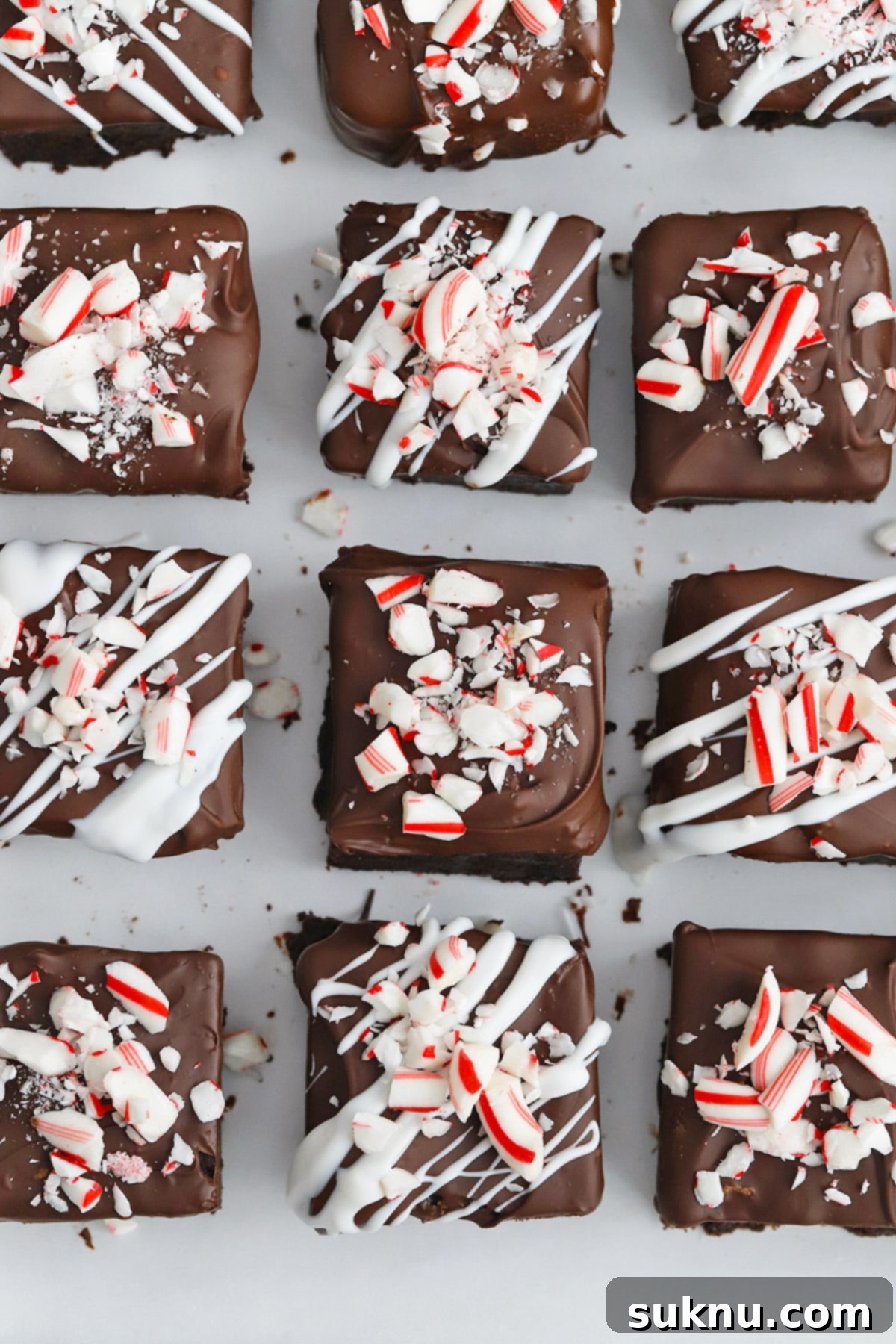 Overhead view of several finished gluten-free peppermint brownie bites, freshly dipped in chocolate and sprinkled with crushed candy canes on parchment paper, ready to set.