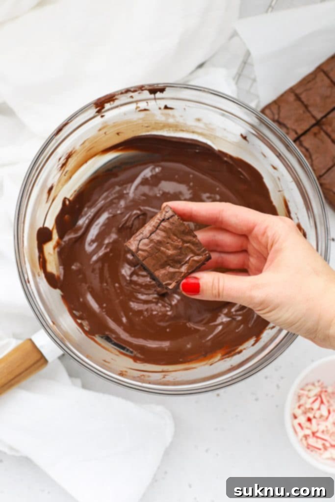 A gluten-free brownie bite being carefully dipped into a bowl of melted dark chocolate with a fork, illustrating the coating process.