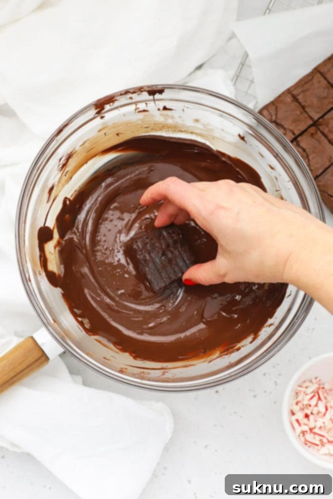 Close-up of a brownie bite fully coated in melted chocolate, with excess chocolate smoothly dripping off, indicating a perfect consistency for dipping.