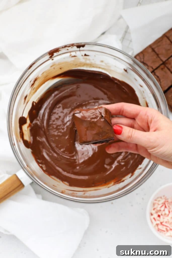 A chocolate-dipped gluten-free brownie bite being transferred from the melted chocolate to a parchment-lined baking sheet, ready for its topping.