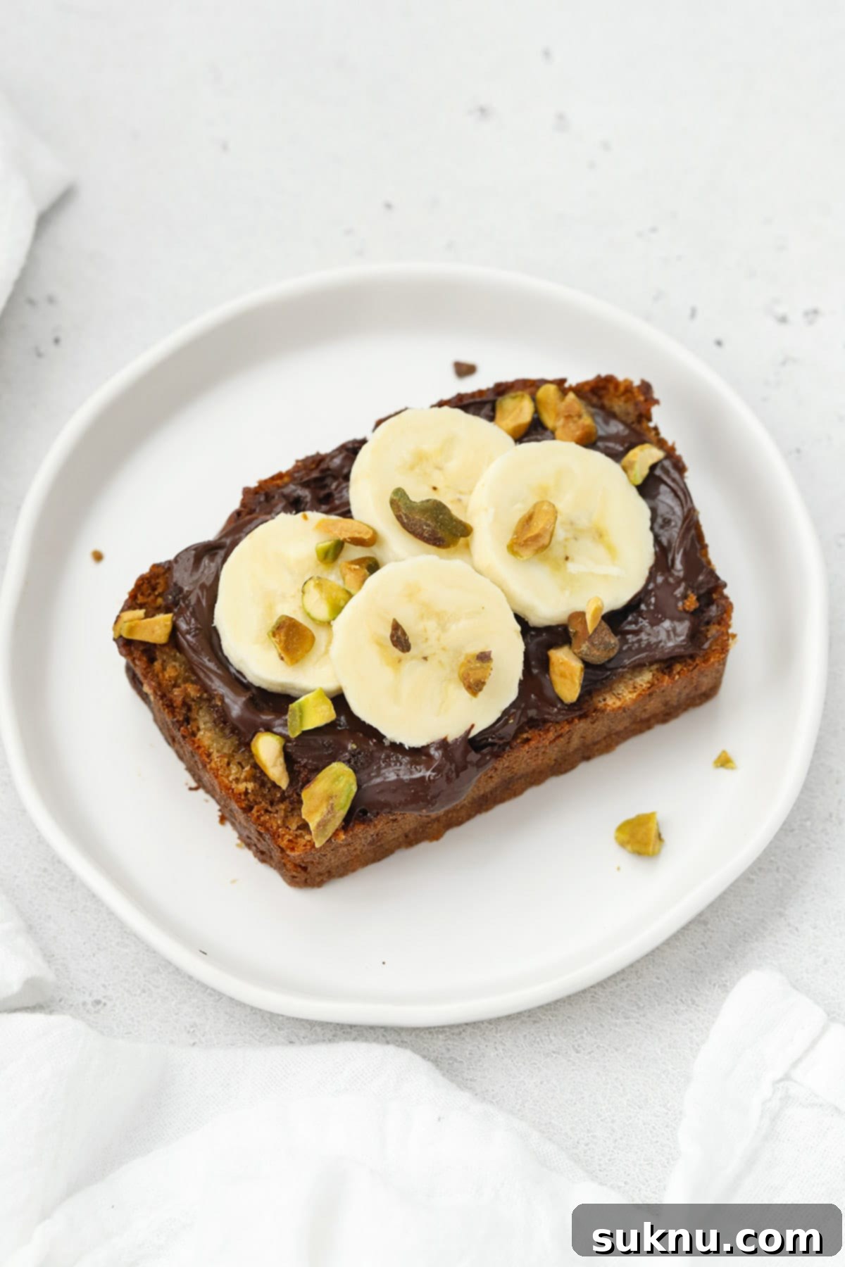 Close-up of a delicious slice of gluten-free banana bread with Nutella, banana, and pistachios.