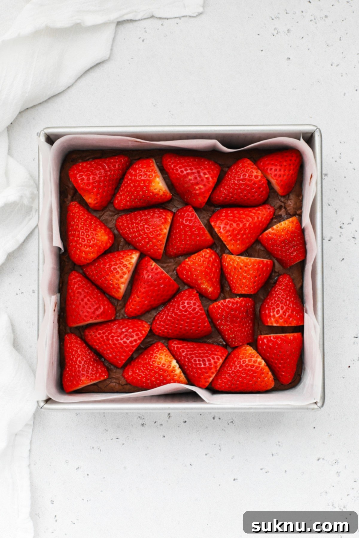 Overhead view of cooled gluten-free brownies topped with neatly arranged, sliced fresh strawberries, ready for the ganache layer.
