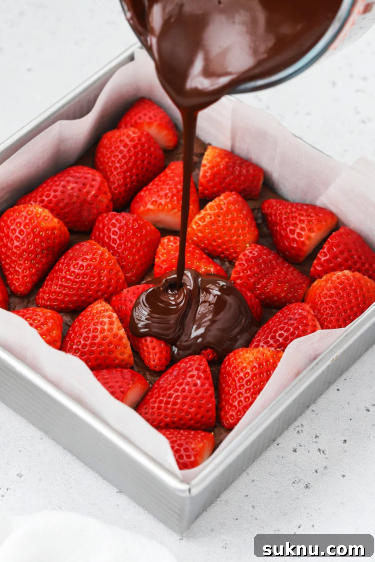 Front view of rich chocolate ganache being poured smoothly over the layer of fresh strawberries on gluten-free chocolate covered strawberry brownies.