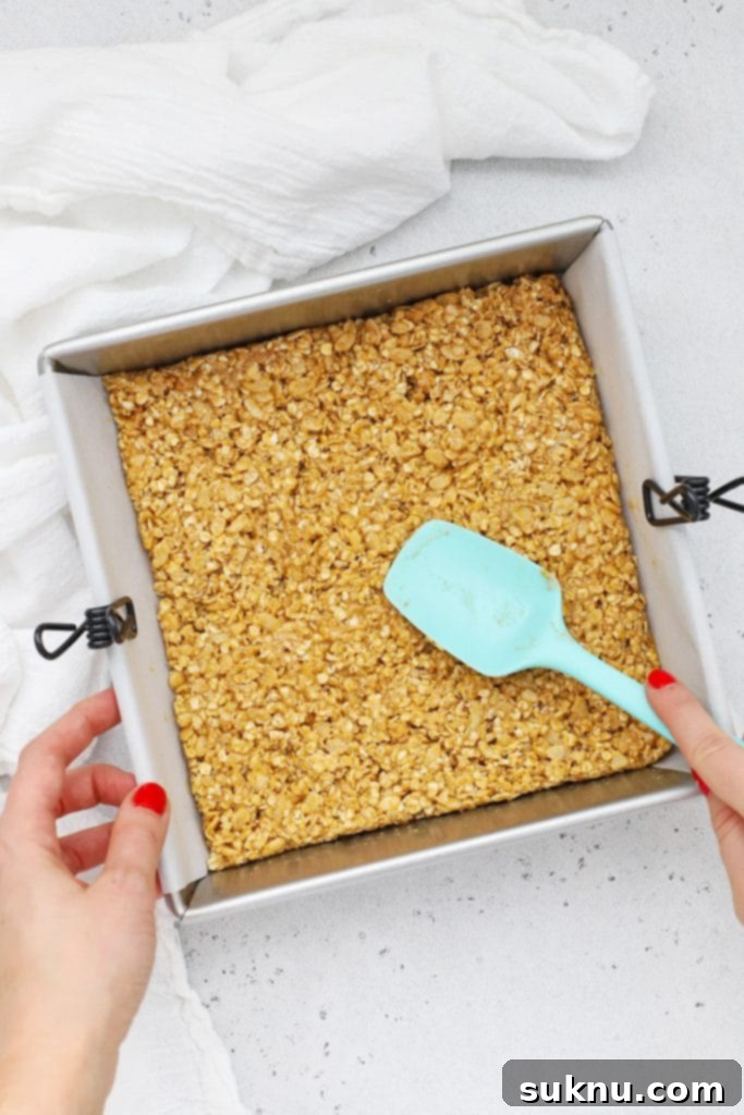 Patting down peanut butter granola bar mixture into an 8x8 baking dish