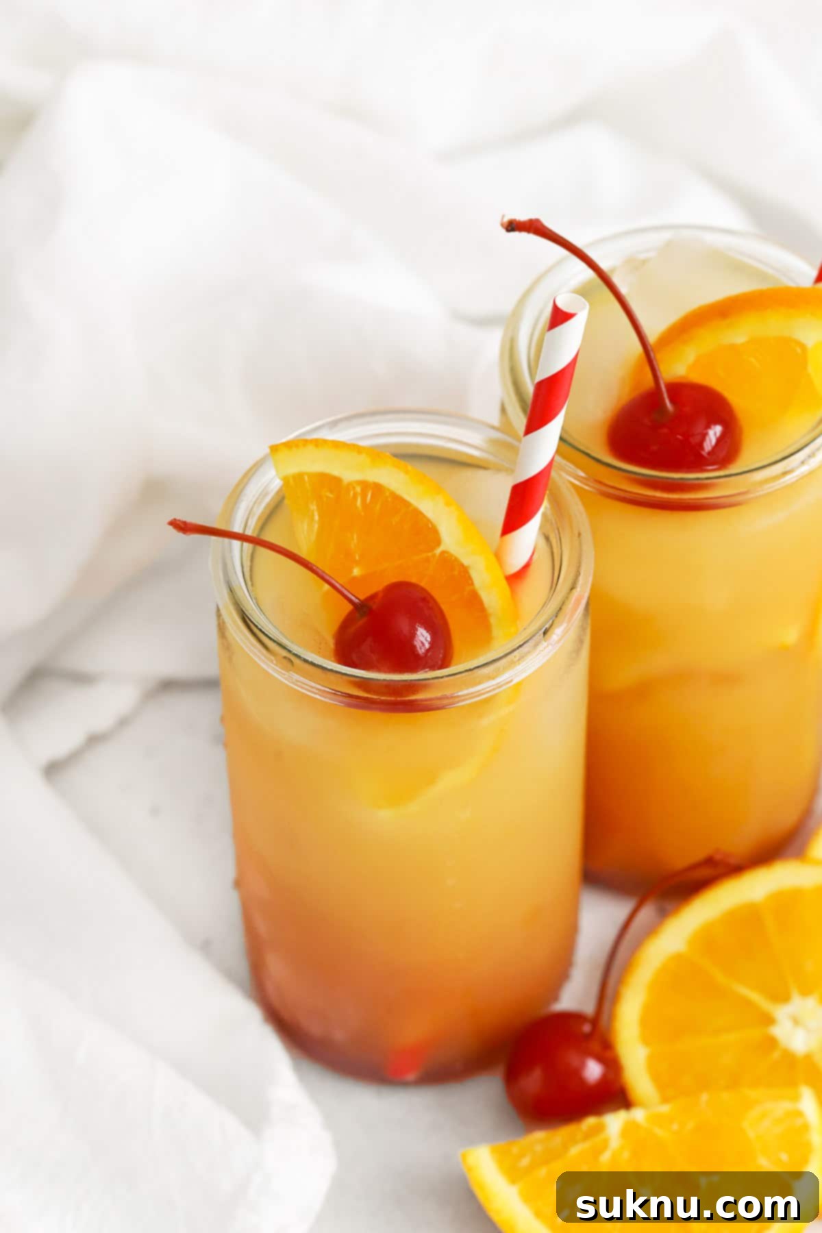Front view of a beautifully layered virgin sunrise mocktail garnished with an orange slice and maraschino cherry