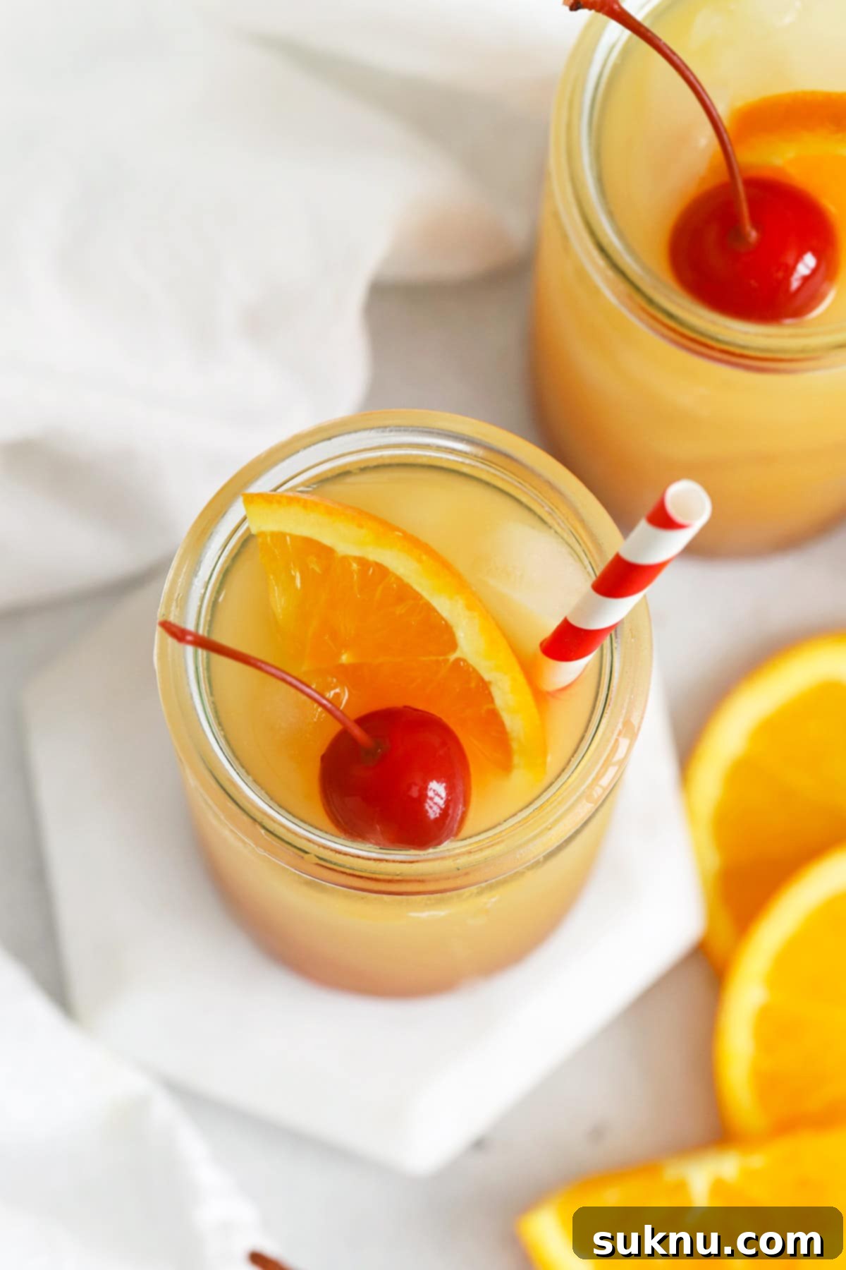 A beautifully garnished Sweets & Thank You Sweet Sunrise Mocktail with an orange slice and maraschino cherry