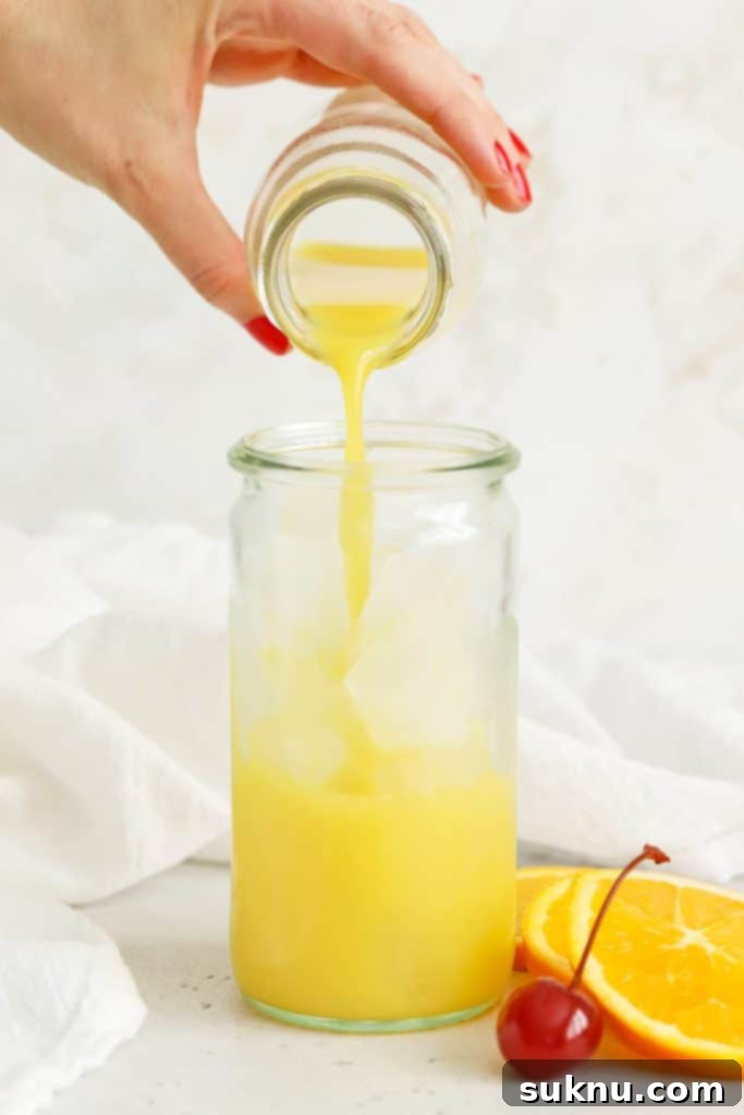 Pouring fresh orange juice over ice for an orange grenadine mocktail