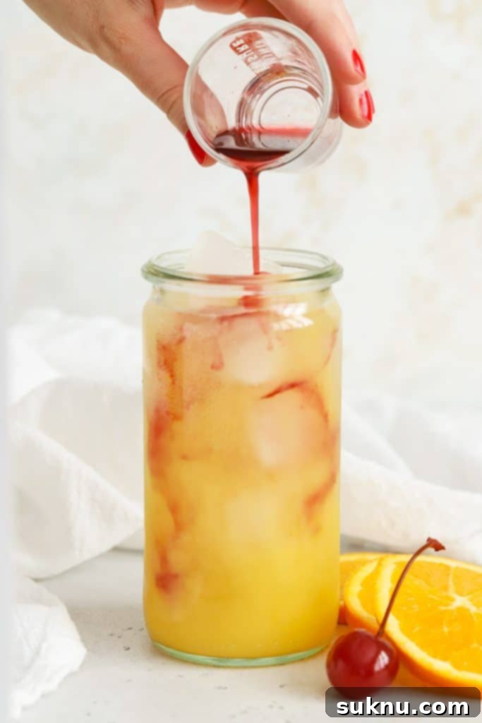 Carefully pouring grenadine over the orange juice and soda mix to create a sweet sunrise mocktail layer