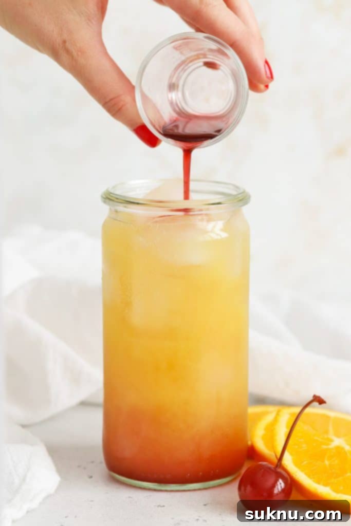 The grenadine syrup slowly sinking through the orange juice to form the sunrise effect in a mocktail