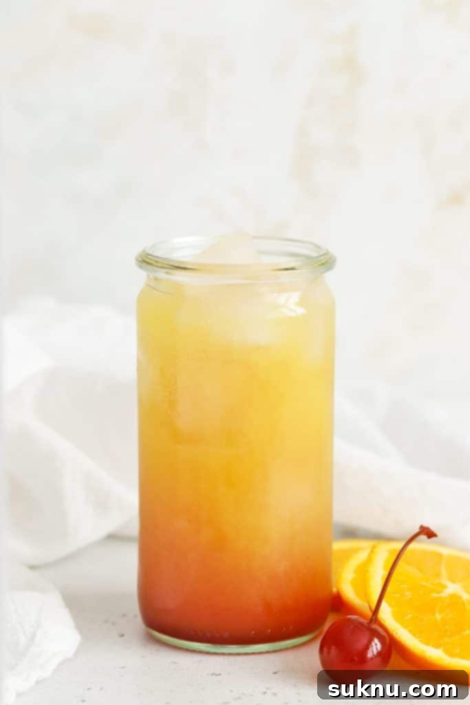 A completed Sweets & Thank You Sweet Sunrise Mocktail, garnished with an orange slice and maraschino cherry, showcasing the beautiful gradient