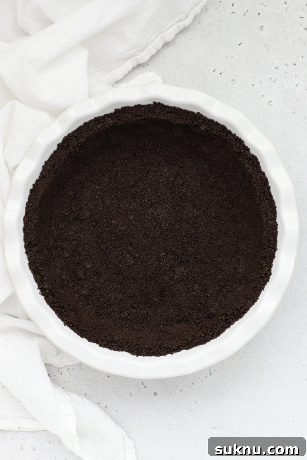 Overhead view of a perfectly baked gluten-free Oreo crust in a pristine white pie pan, ready for filling