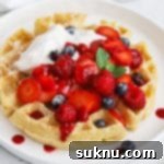 Front view of gluten-free Belgian waffles topped with berries, whipped cream, and raspberry syrup