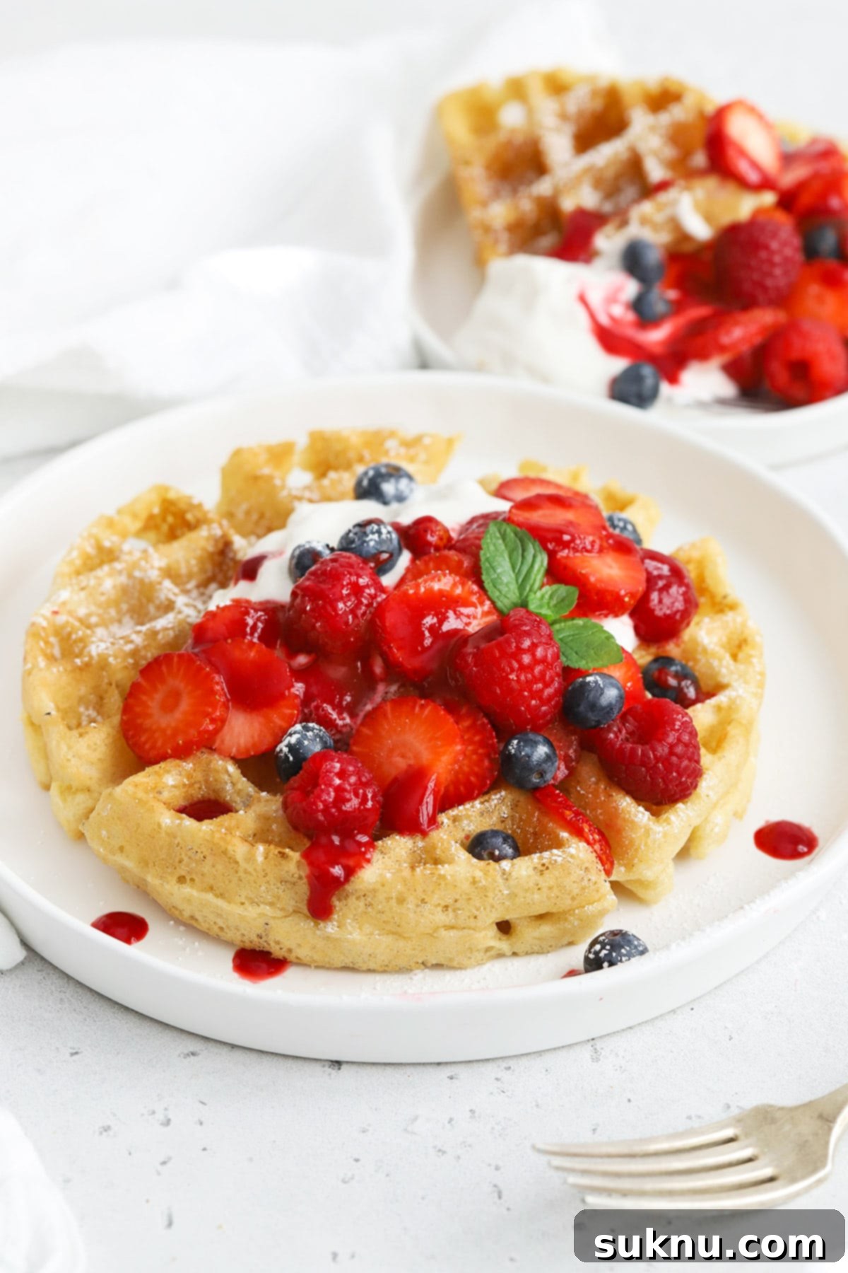 Front view of gluten-free Belgian waffles lavishly topped with berries, whipped cream, and a drizzle of raspberry syrup