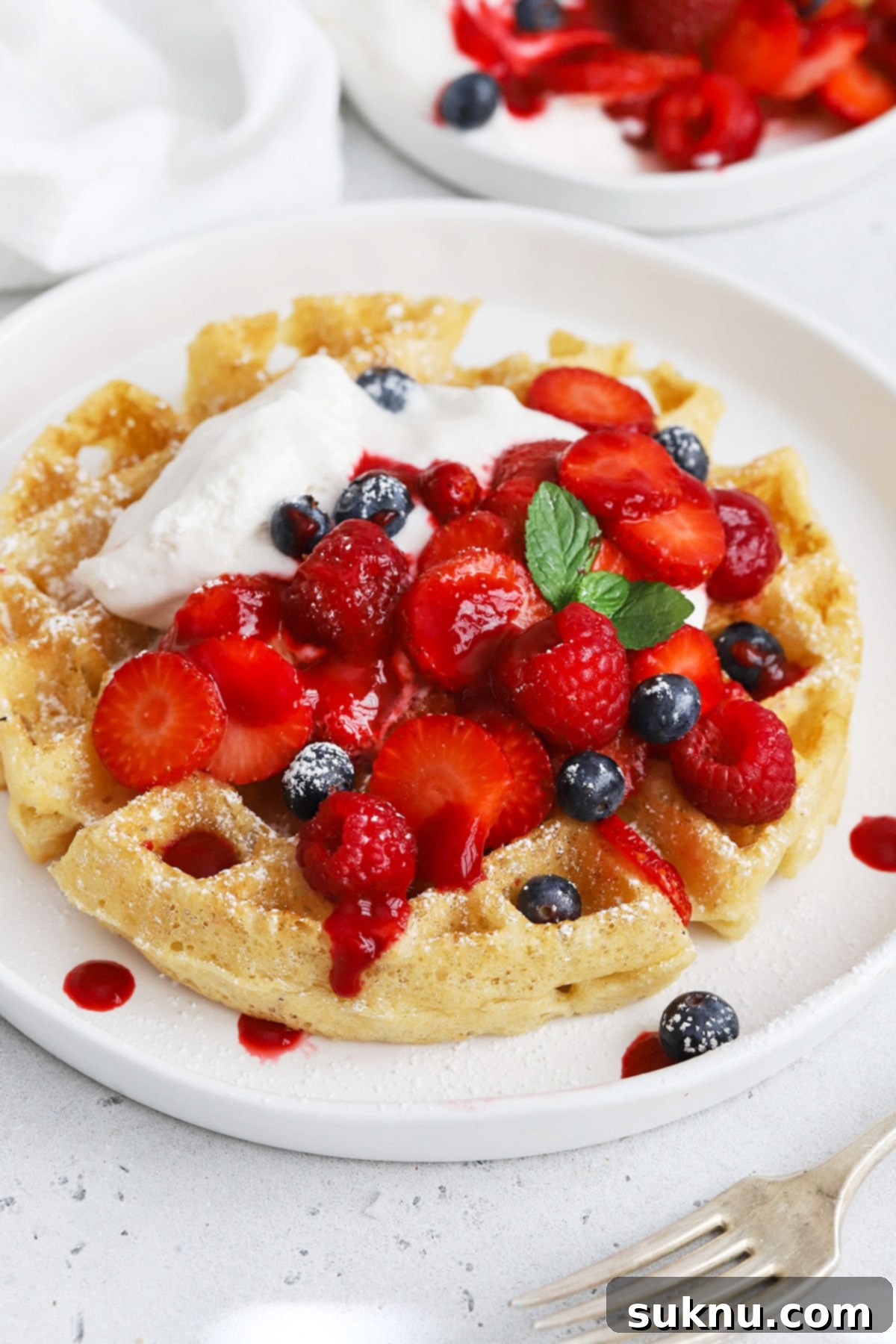 Front view of gluten-free Belgian waffles generously topped with berries, whipped cream, and raspberry syrup, ready to be served