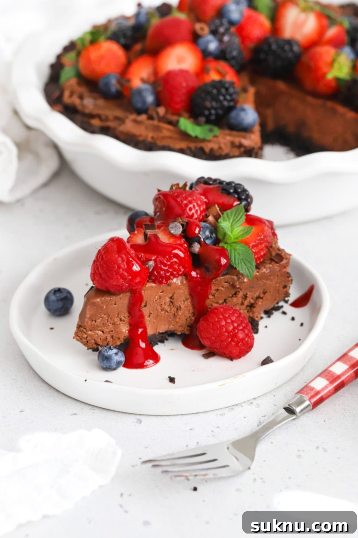 Front view of a slice of no-bake gluten-free chocolate cheesecake pie with fresh berries and raspberry sauce