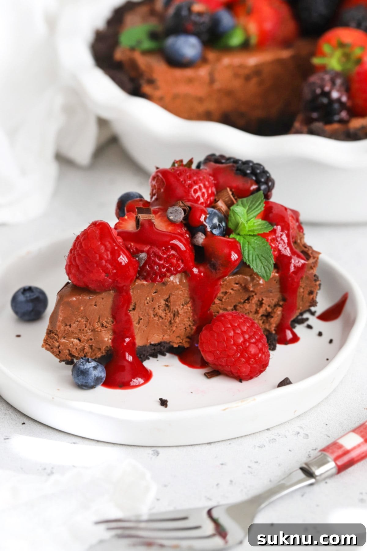 Front view of a slice of no-bake gluten-free chocolate cheesecake pie with fresh berries and raspberry sauce