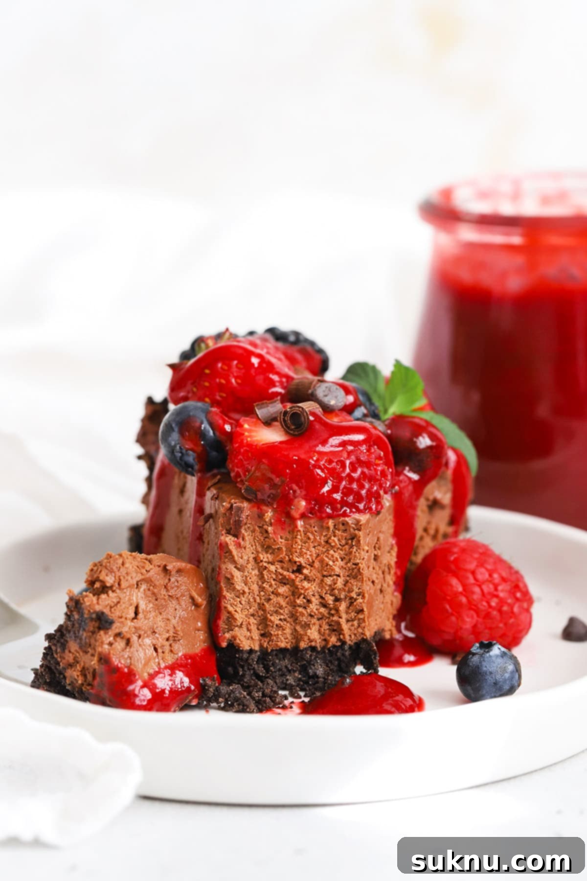 Front view of a slice of no-bake gluten-free chocolate cheesecake pie with fresh berries and raspberry sauce