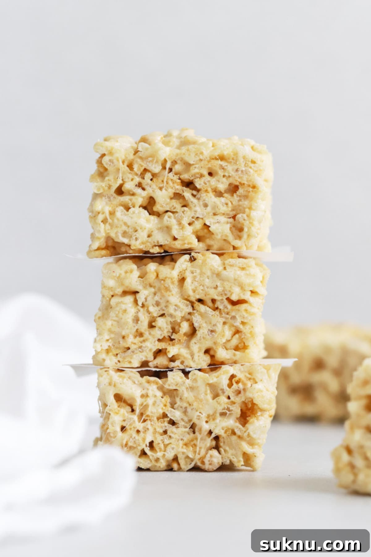 Three golden brown butter rice krispies treats stacked on top of each other, sprinkled with flaky sea salt.