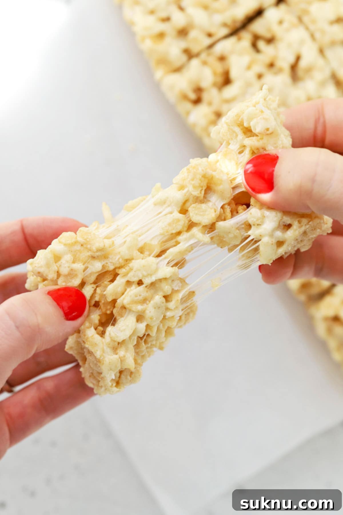 A close-up of a gluten-free brown butter rice krispies treat being pulled apart, highlighting its irresistible stretchiness.