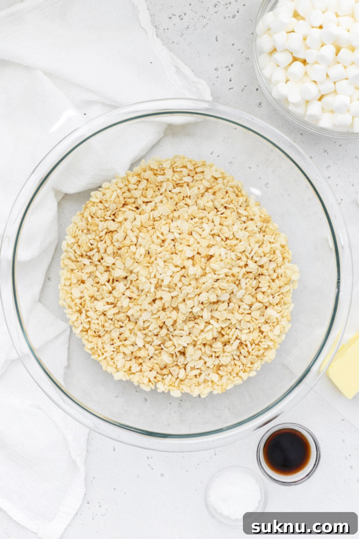 Overhead view of five ingredients: gluten-free crispy rice cereal, butter, mini marshmallows, vanilla extract, and flaky sea salt.