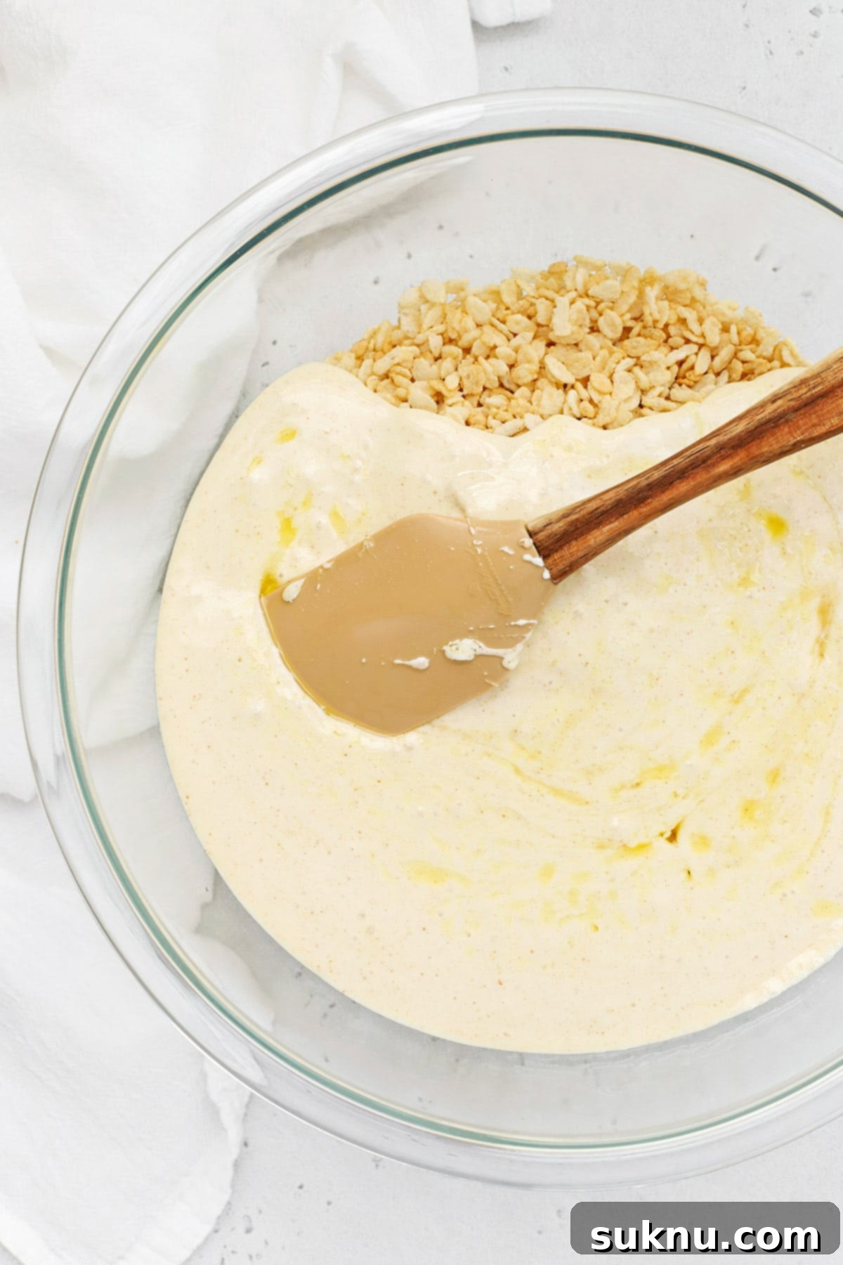 A spatula gently stirring the marshmallow mixture into the gluten-free crispy rice cereal, ensuring even coating.