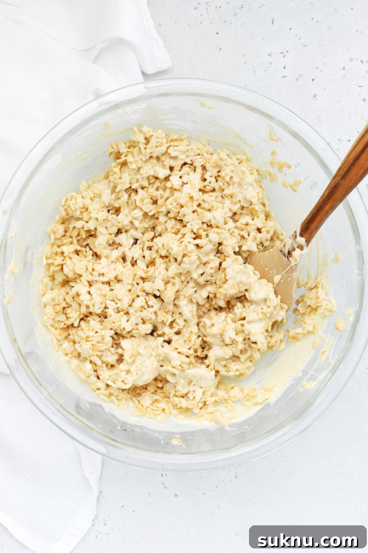 The fully combined gluten-free brown butter rice krispies treat mixture being pressed into a parchment-lined baking pan.