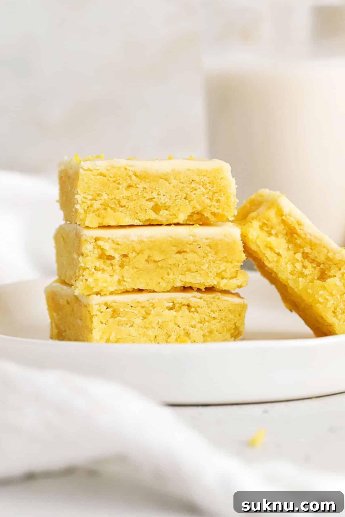 Stacked fudgy gluten-free lemon brownies on a white plate, beautifully frosted with a vibrant lemon glaze