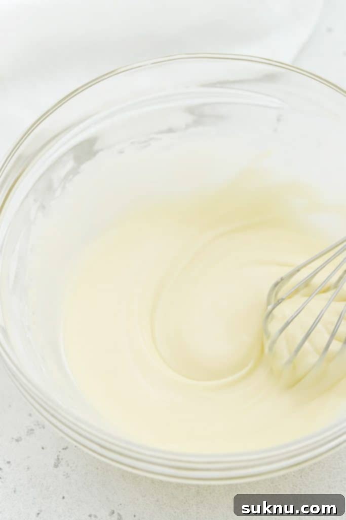 Lemon glaze being whisked in a bowl until smooth, ready to be poured over the cooled gluten-free lemon brownies.