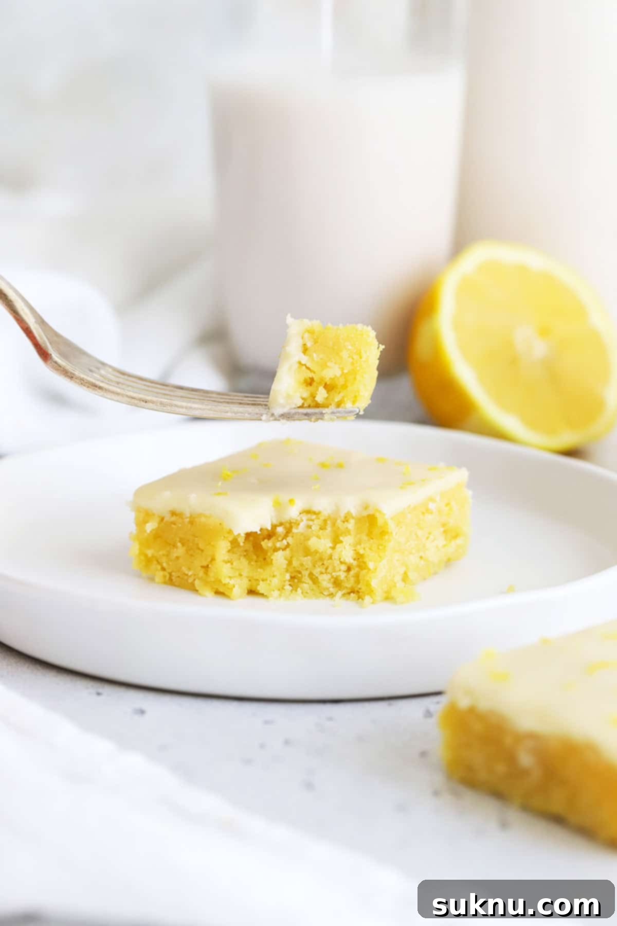 Close-up front view of a gluten-free lemon brownie with a bite taken, revealing its incredibly fudgy, dense, and moist texture beneath the bright lemon glaze.