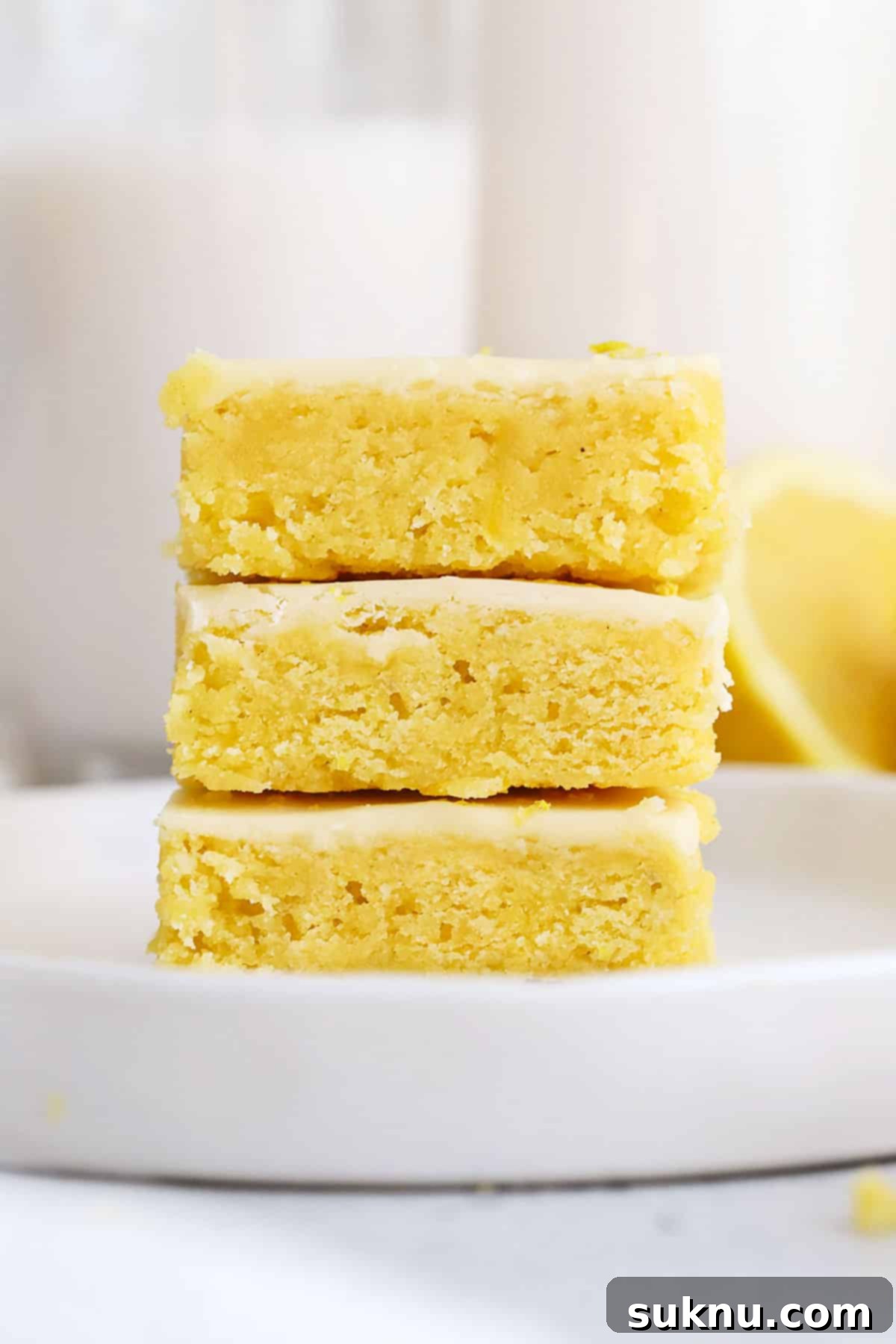A stack of three perfectly frosted gluten-free lemon brownies on a white plate, ready to be enjoyed.