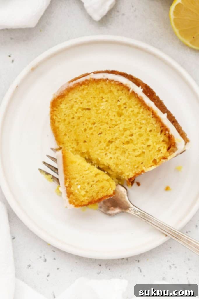 A delightful slice of gluten-free lemon bundt cake on a white plate, drizzled with a sweet glaze and garnished with lemon zest.