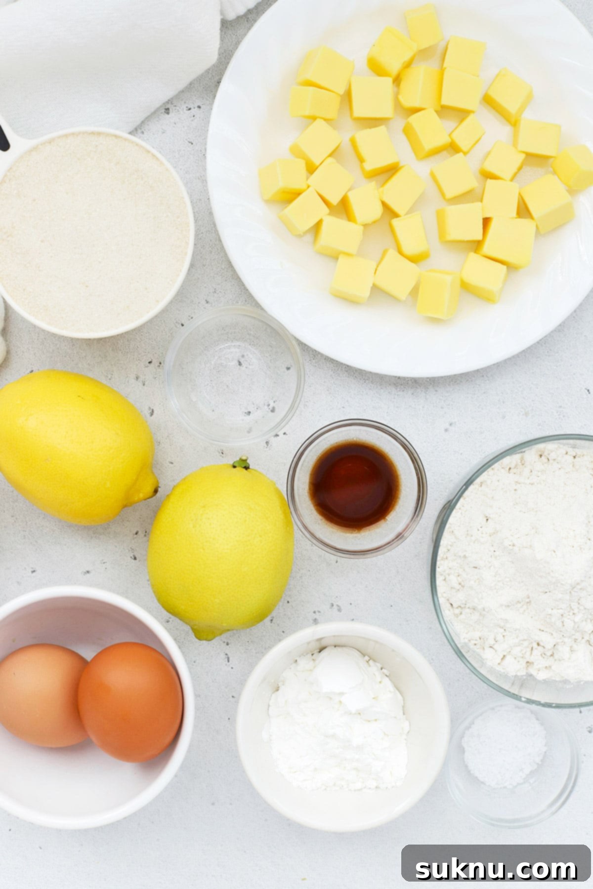 A selection of fresh ingredients laid out for baking gluten-free lemon brownies, including lemons, butter, sugar, and flour