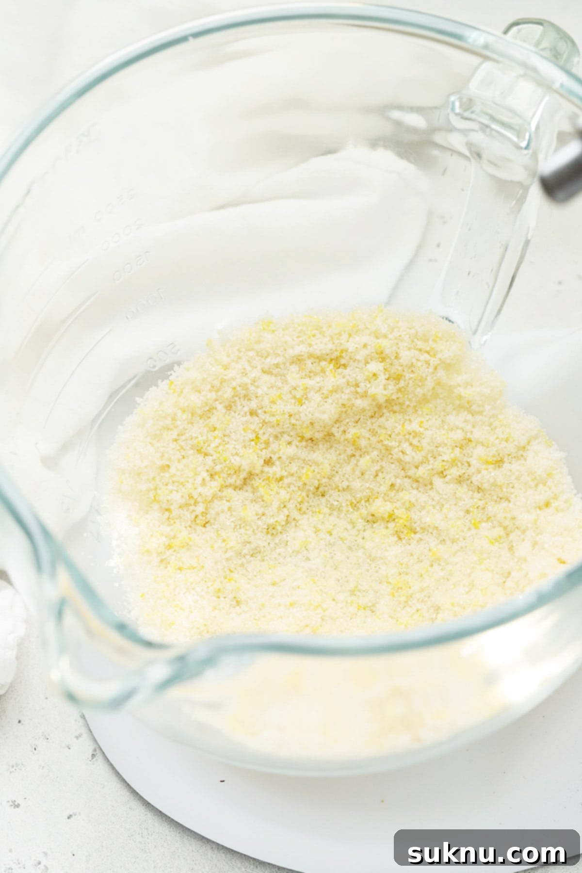 Close-up of lemon zest being rubbed into granulated sugar in a mixing bowl, creating a fragrant, yellow mixture.