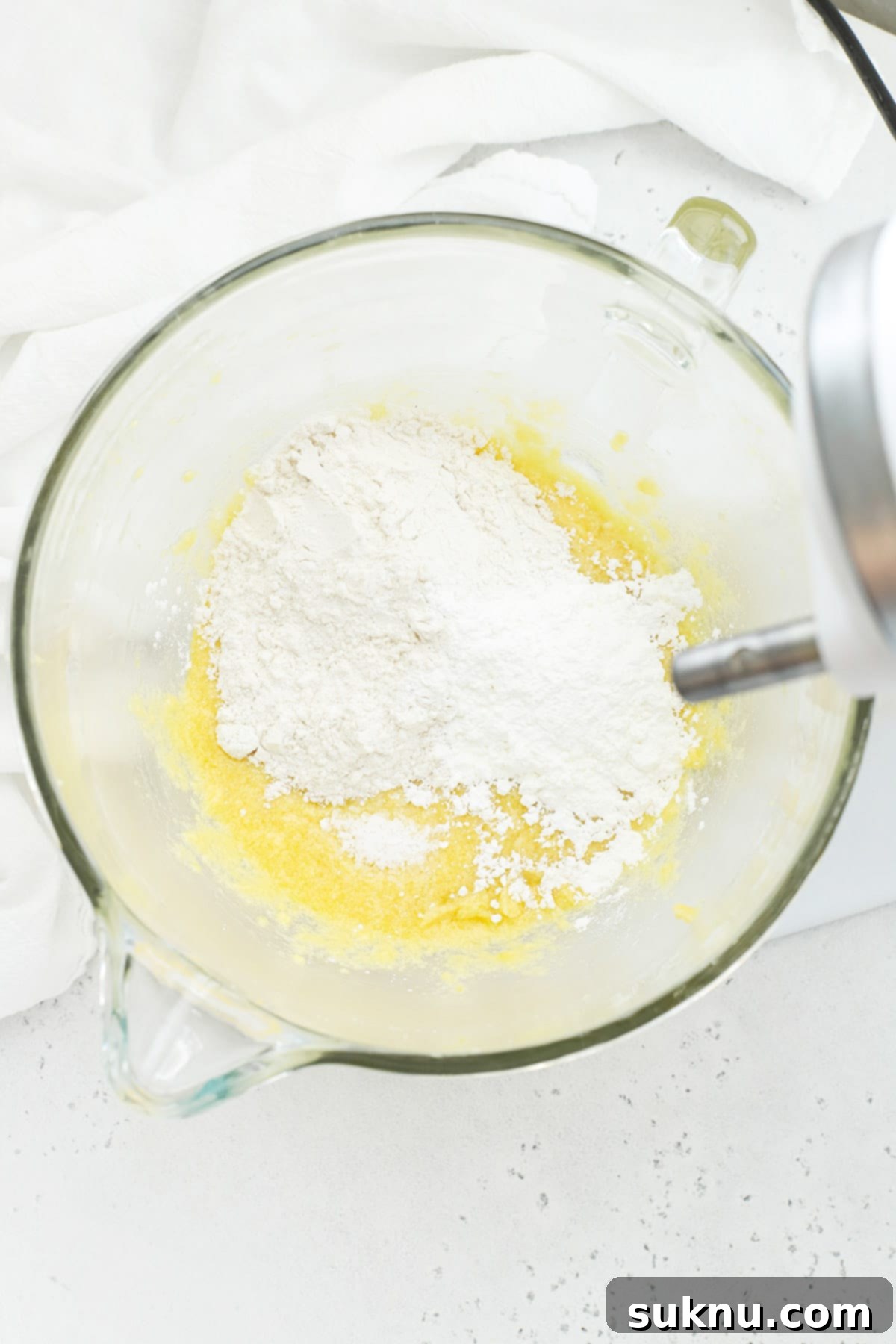 Dry ingredients, including gluten-free flour and cornstarch, being added to the wet mixture for gluten-free lemon brownie batter.