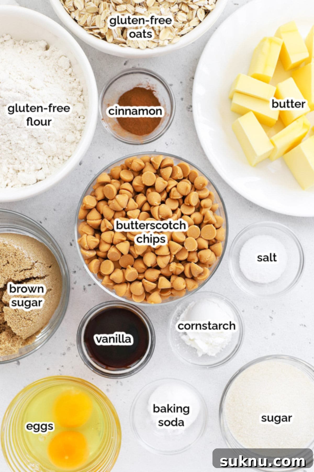 A selection of ingredients laid out for making gluten-free oatmeal scotchies, including butter, sugars, eggs, flour, oats, and butterscotch chips.
